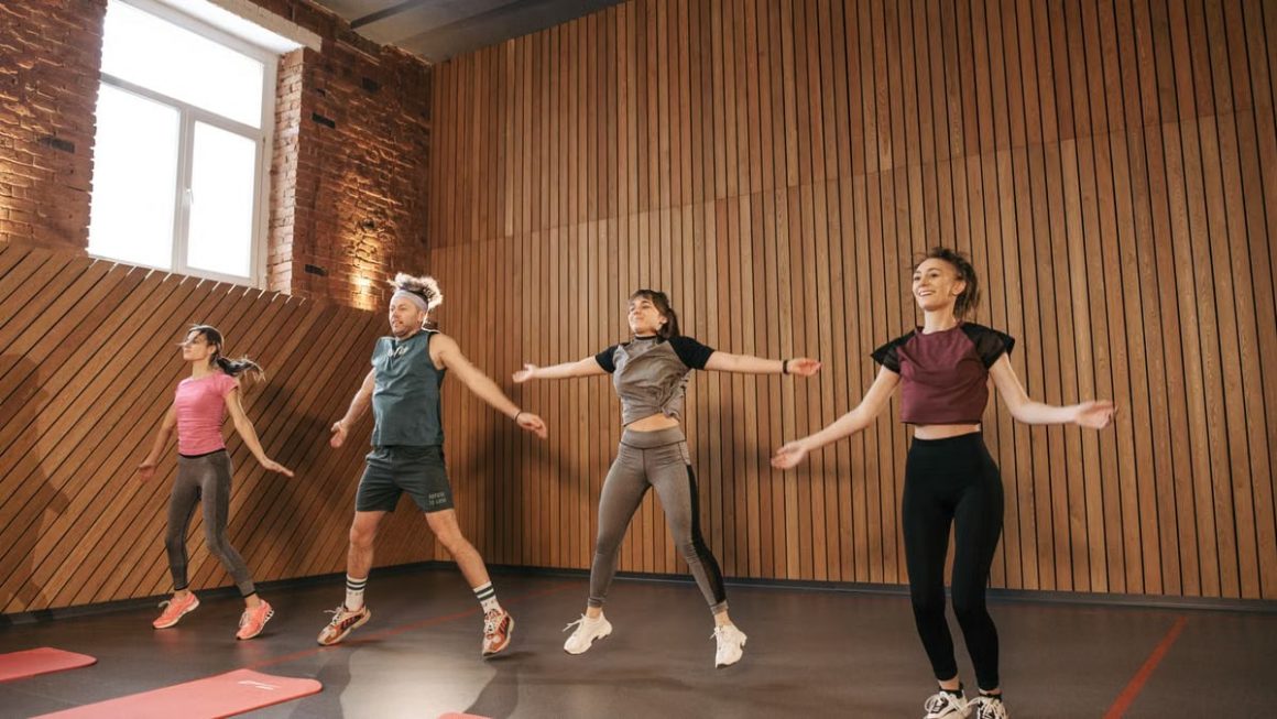 Group of adults doing jumping jacks in modern gym interior.