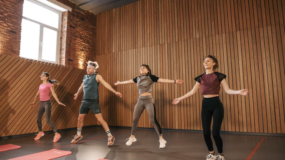 Group of adults doing jumping jacks in modern gym interior.