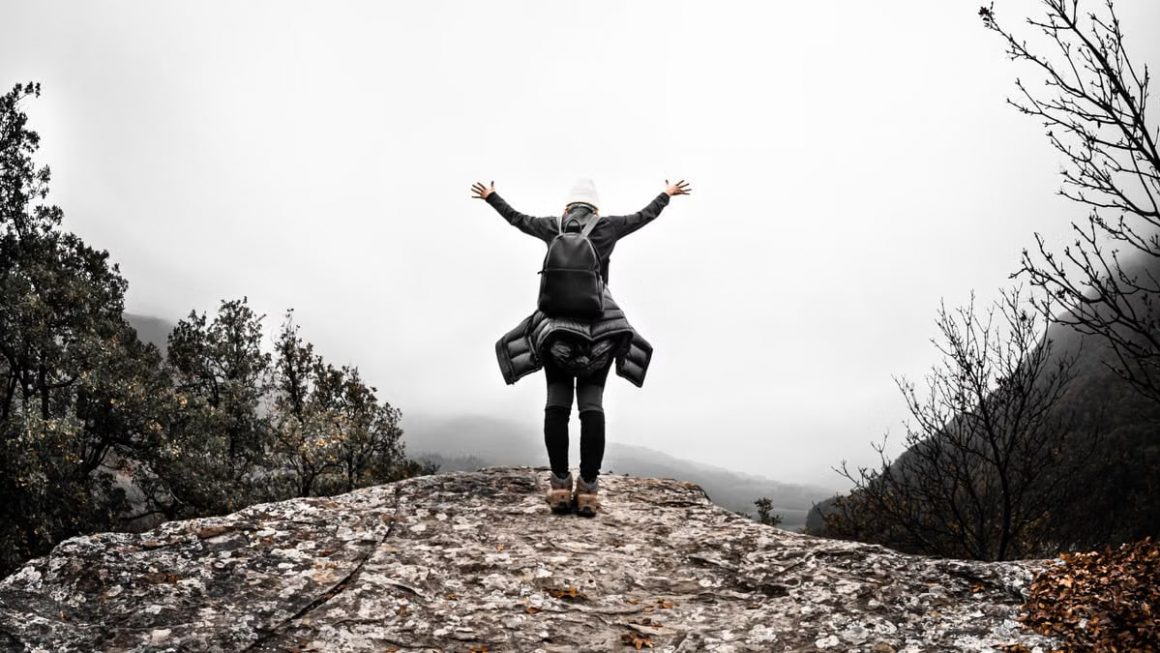 Person with arms raised on rocky mountain top, celebrating freedom and nature's beauty.