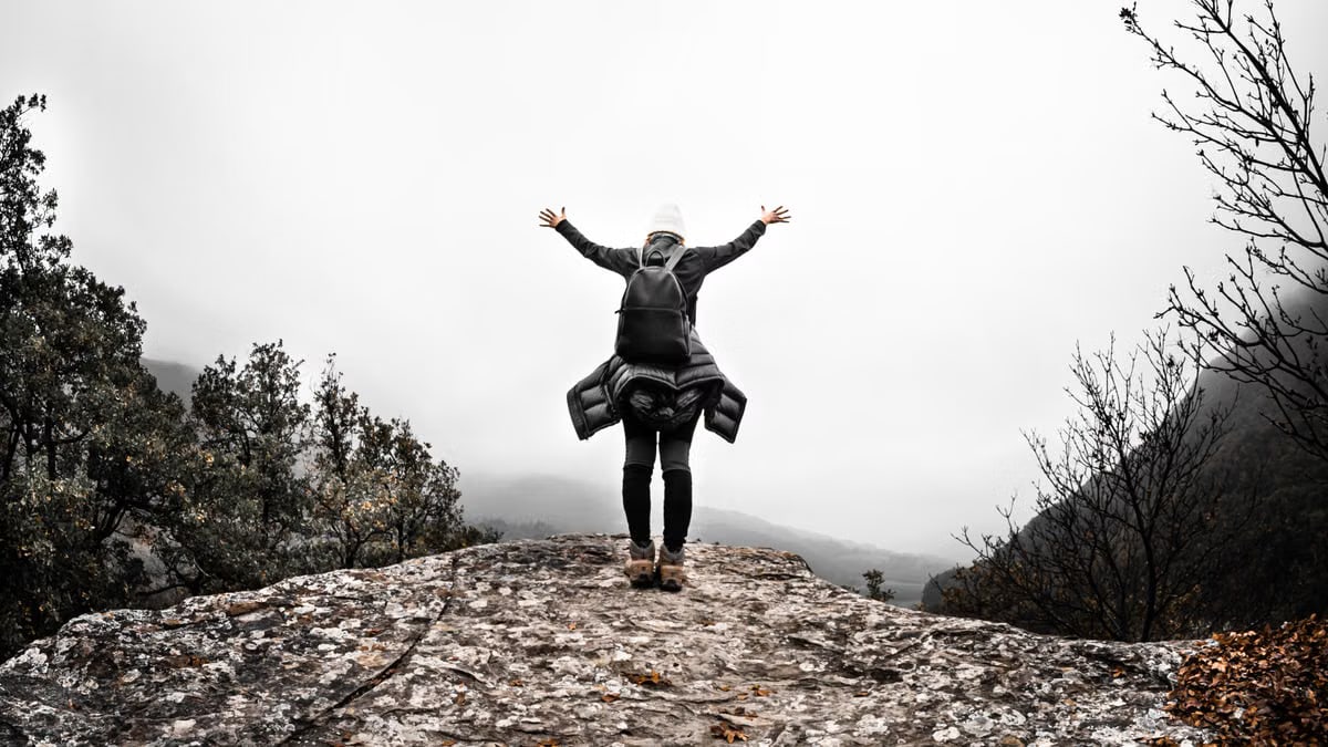 Person with arms raised on rocky mountain top, celebrating freedom and nature's beauty.